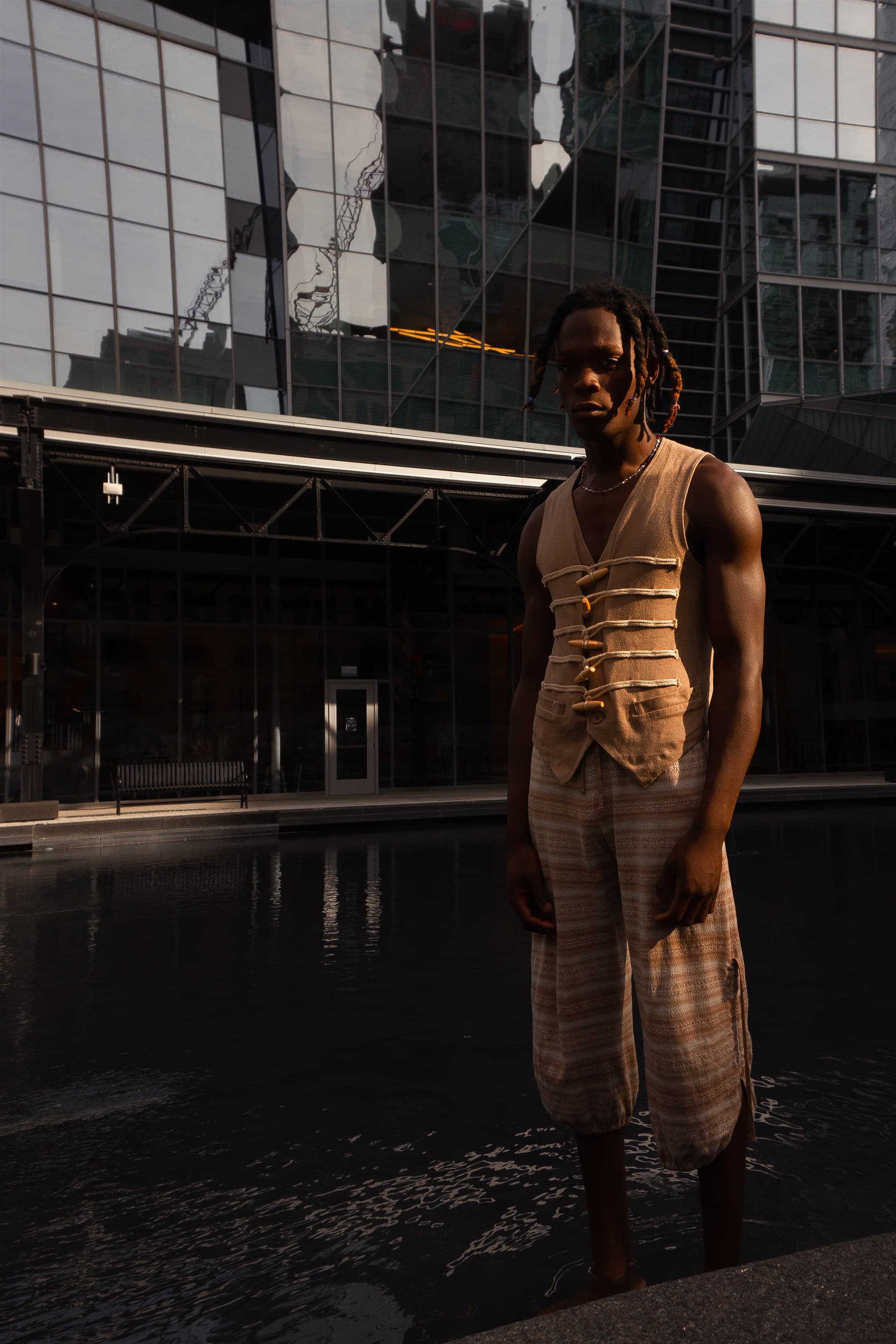 A model in a layered vest and striped trousers photographed against a glass facade