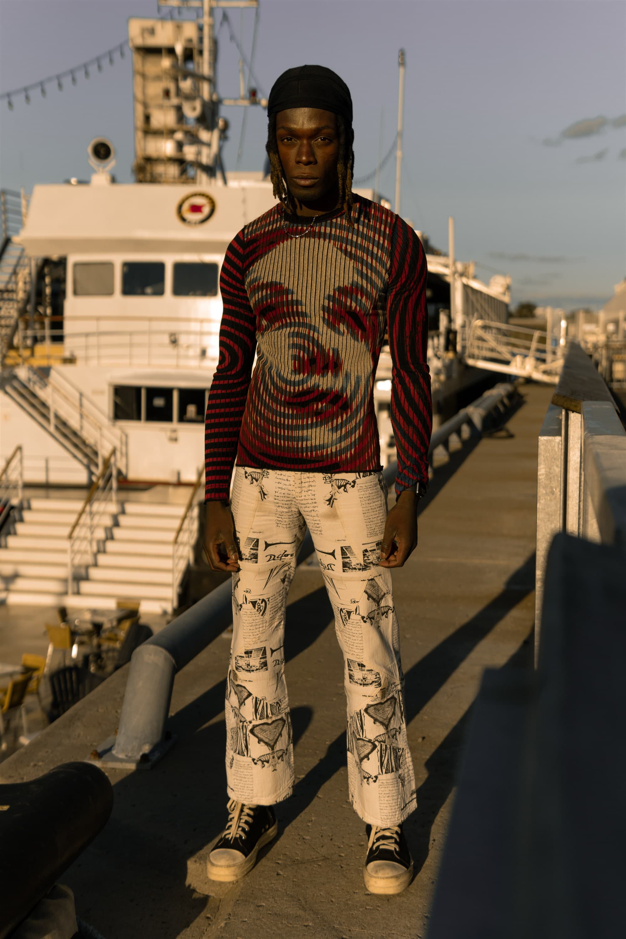 A model in a Jean Paul Gaultier printed knit standing on a dock at golden hour
