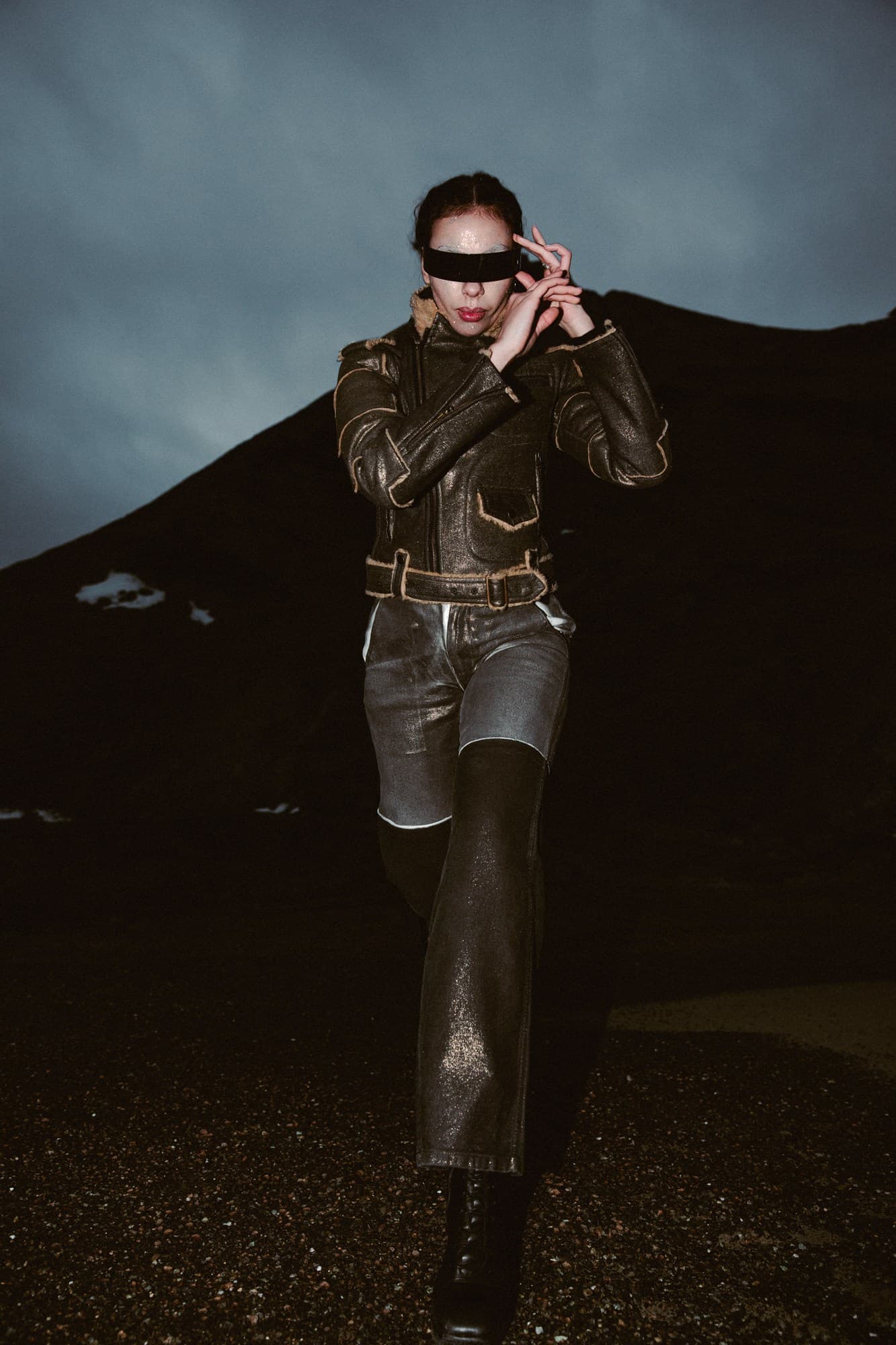A model in a visor and distressed leather jacket walking toward the camera at dusk
